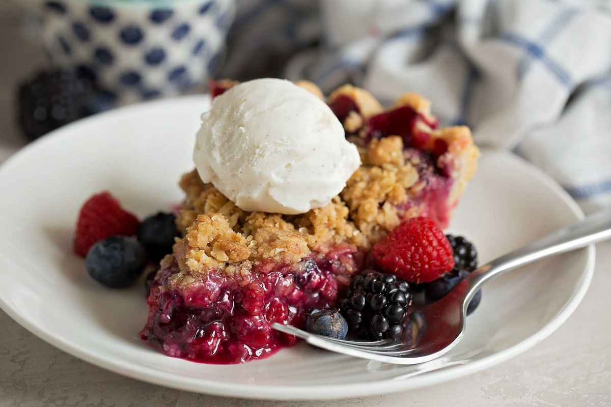 Berry Pie topped with ice cream, served on a white plate.