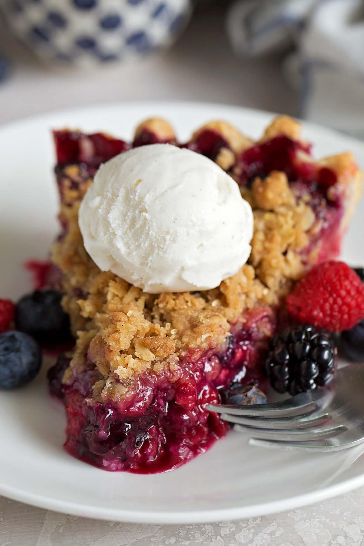 Ice cream topped triple berry pie served on a white plate.