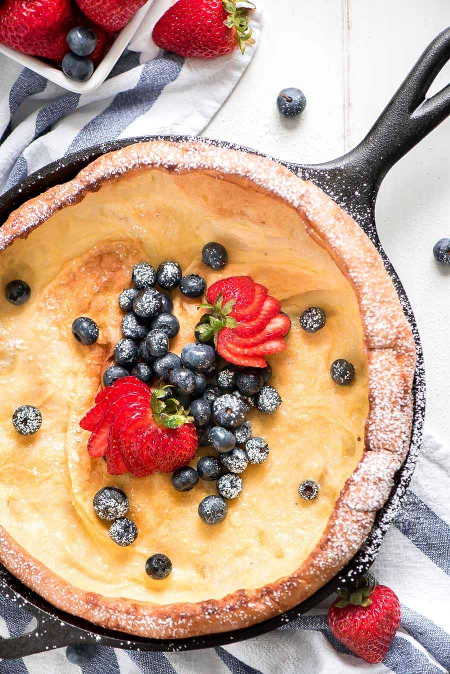 An overhead shot of a Dutch Baby Pancake Recipe in a skillet topped with fresh berries.