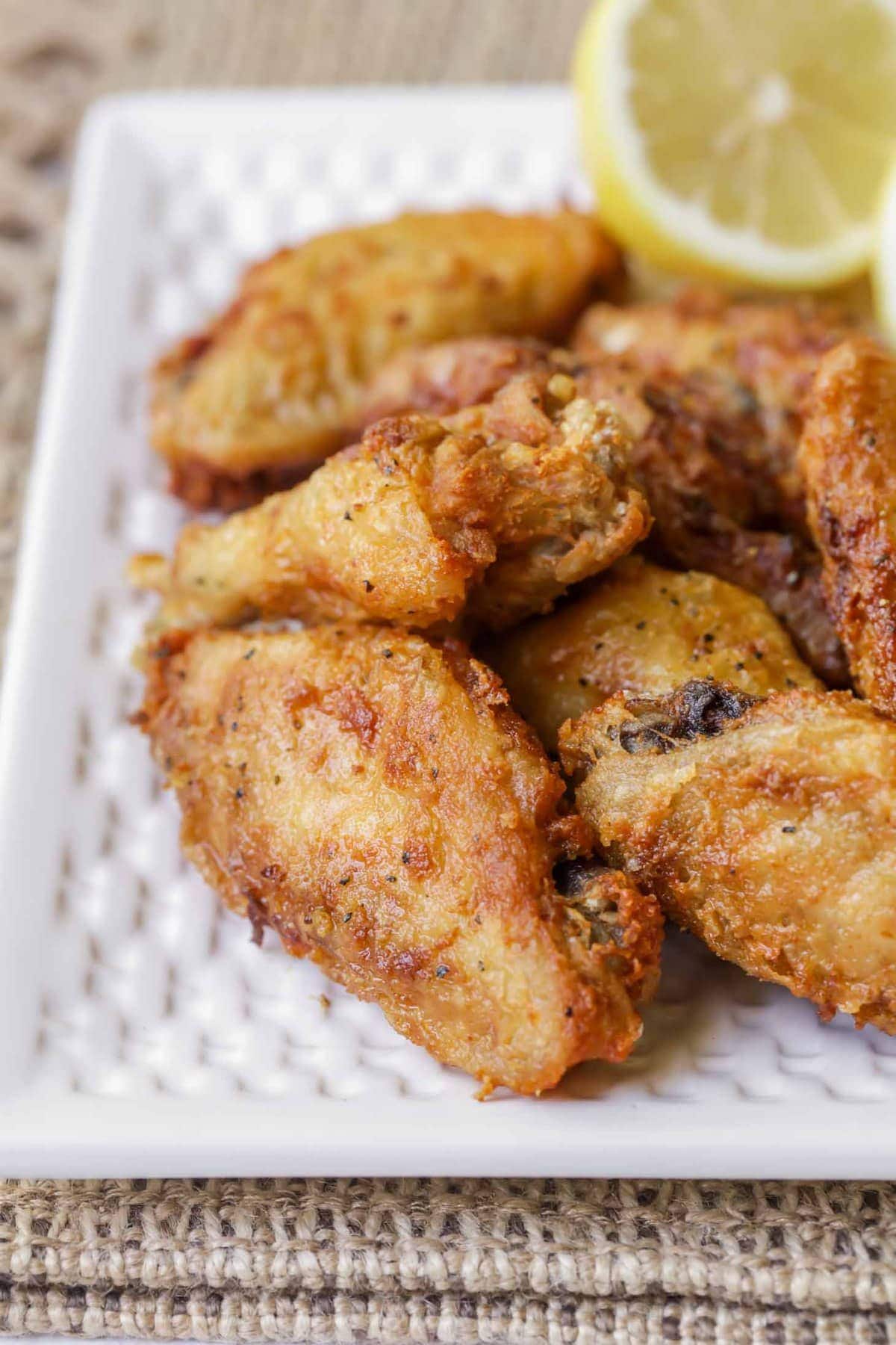 Lemon Pepper Wings stacked on a white plate with lemon slices