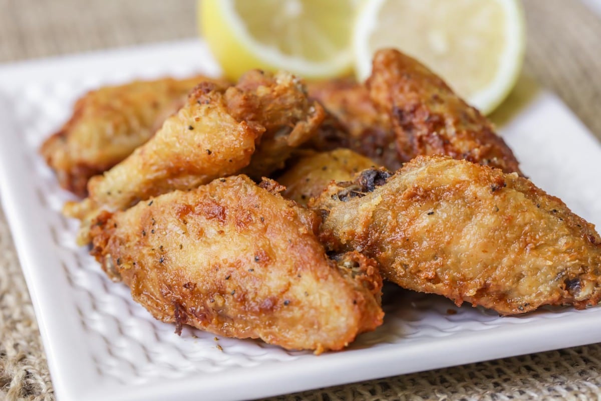 Super Bowl Appetizers - Lemon Pepper Wings garnished with two lemon halves on a white plate. 