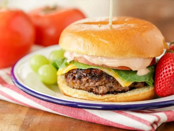 A ranch burger served on a plate with fresh fruit.