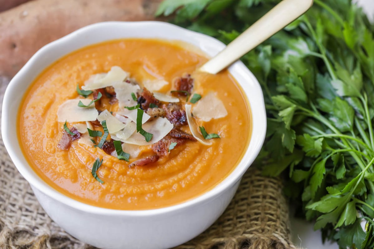 Sweet Potato Soup served in a white bowl and topped with bacon and herbs.