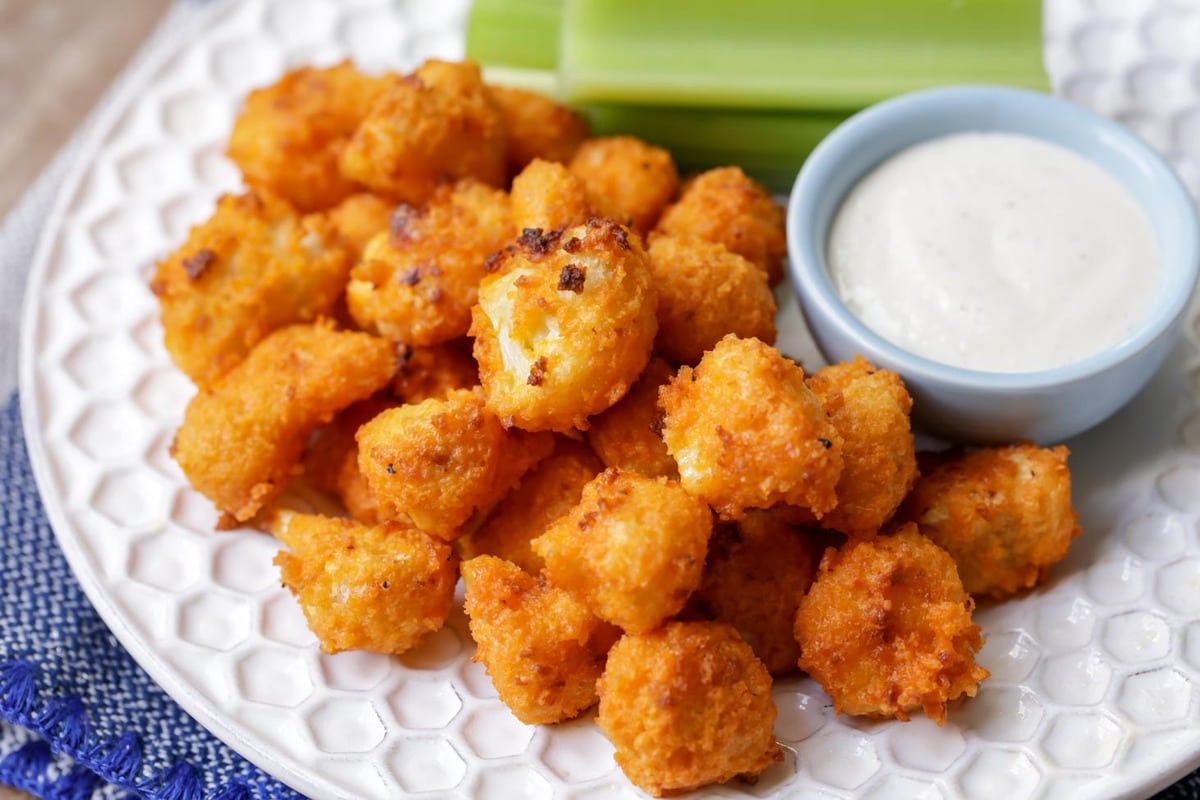 Make these buffalo cauliflower bites for your next football party! No one will even notice they are healthier or even made with cauliflower. They're our new go-to appetizer! Buffalo Cauliflower on plate with ranch and celery