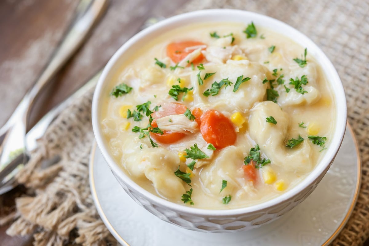 Chicken Dinner Ideas - Chicken dumpling soup in a white bowl topped with fresh herbs.