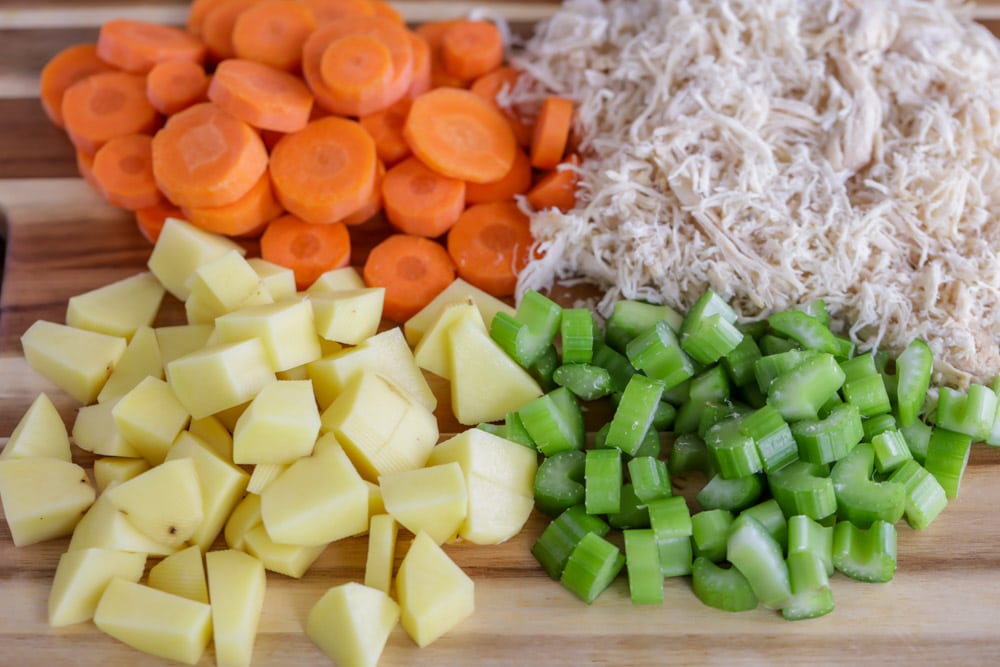 Chopped veggies and shredded chicken on a cutting board.