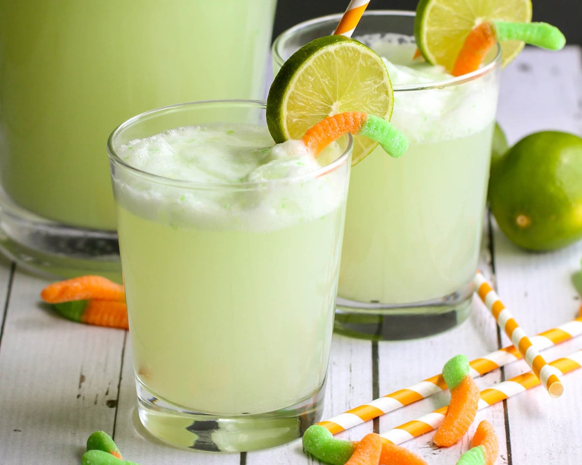 Holiday drink ideas - green witches brew garnished with a gummy worm and lime slice.