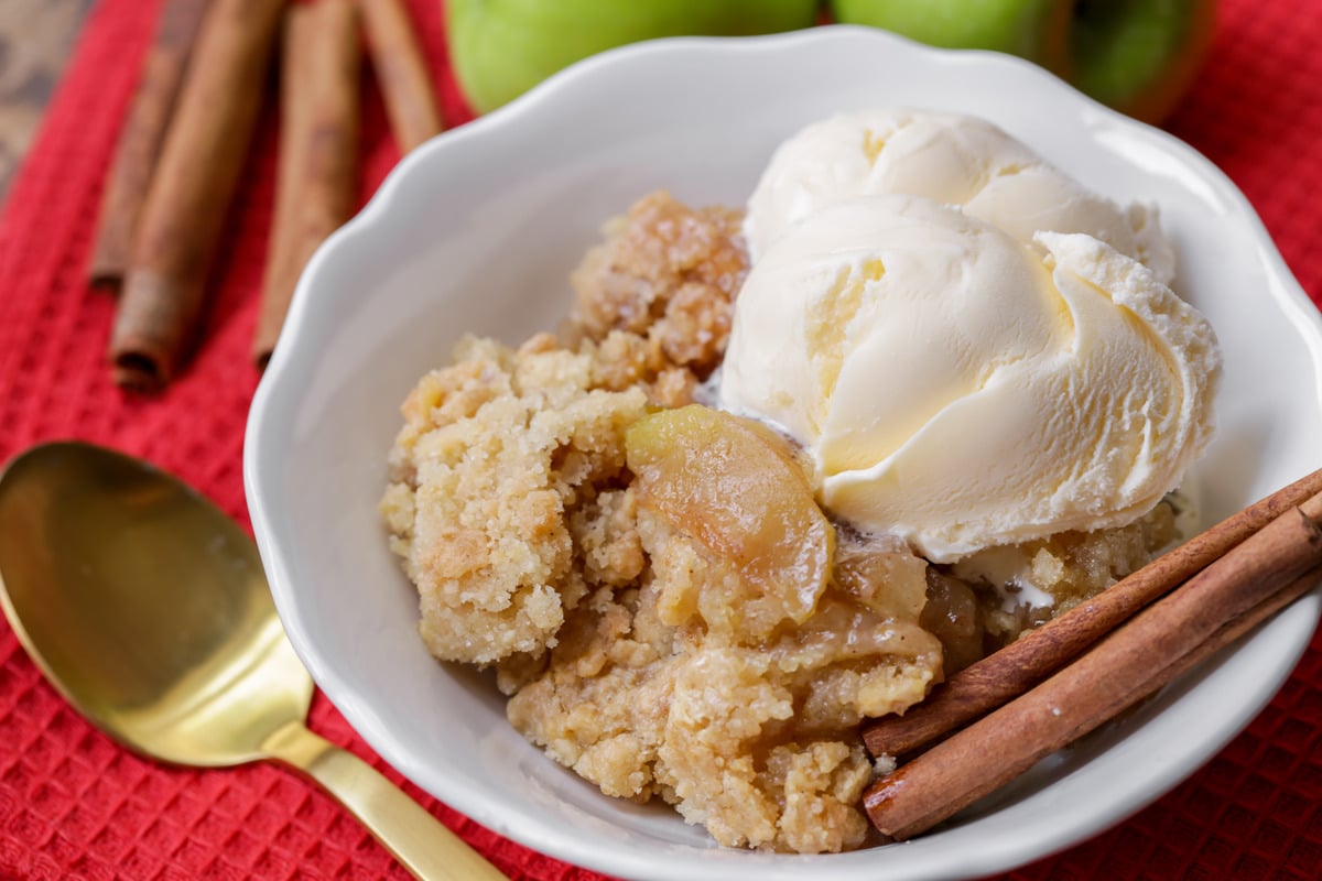 A scoop of apple cobbler topped with vanilla ice cream in a white bowl.