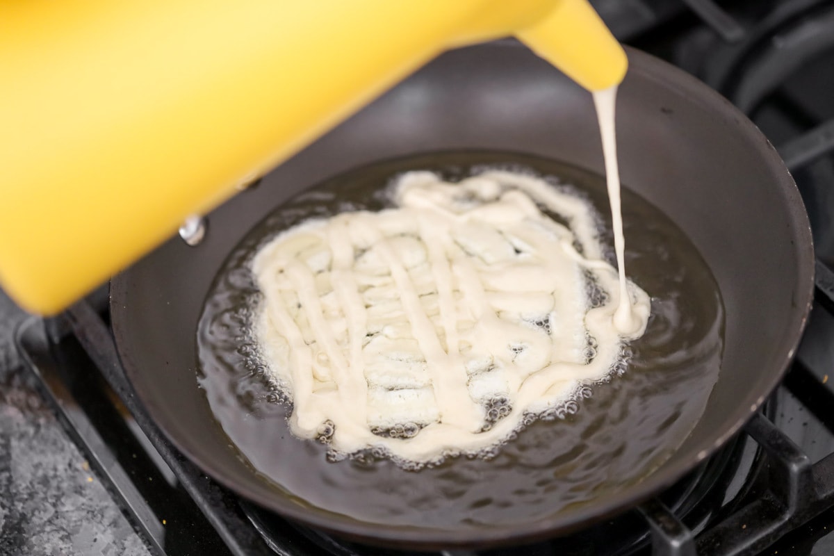 Funneling batter into a pan of hot oil.