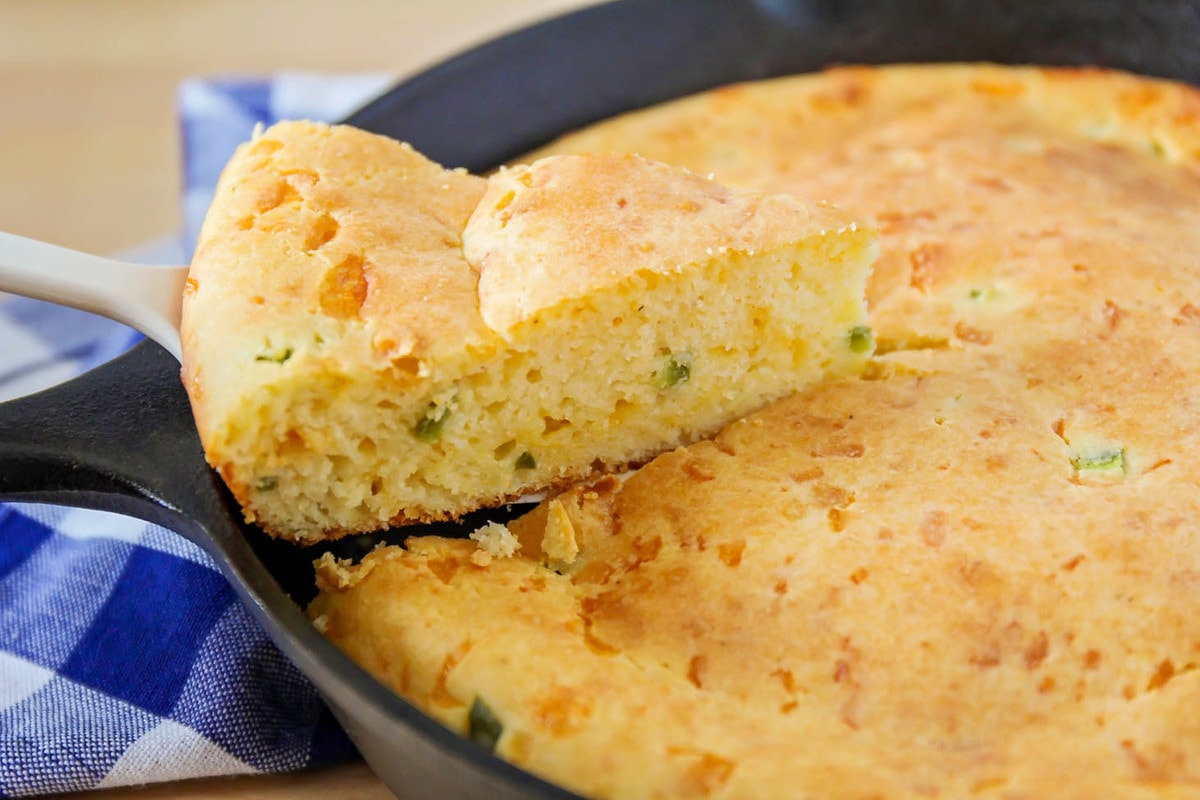 Scooping a slice of jalapeno cornbread from a cast iron skillet.