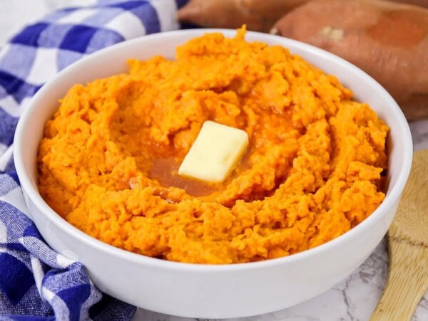 Mashed sweet potatoes prepared in white bowl with butter pat on top.