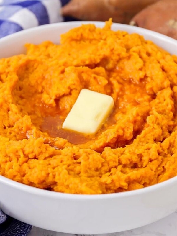 Mashed sweet potatoes prepared in white bowl with butter pat on top.