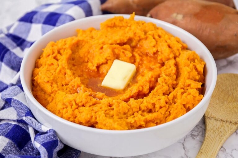 Mashed sweet potatoes prepared in white bowl with butter pat on top.