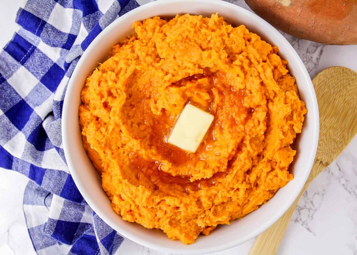 Mashed sweet potatoes in white bowl with butter and syrup on top.