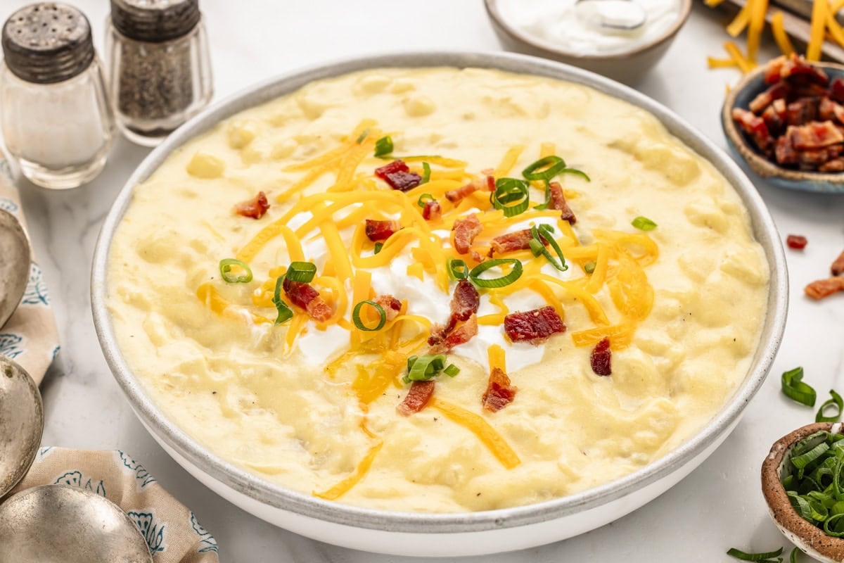 Cheese potato soup in bowl with sour cream, cheese, bacon and scallions on top.