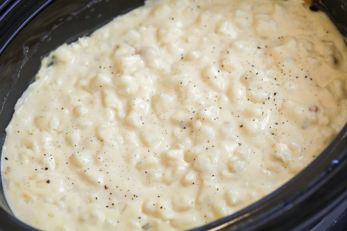 Cream soups and potatoes mixed in a crockpot and topped with pepper.