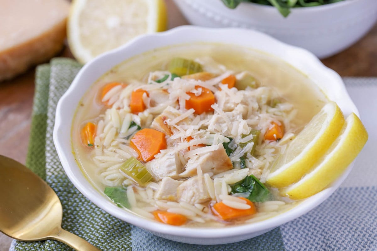 Lemon chicken and orzo soup in a white bowl with two slices of fresh lemon.