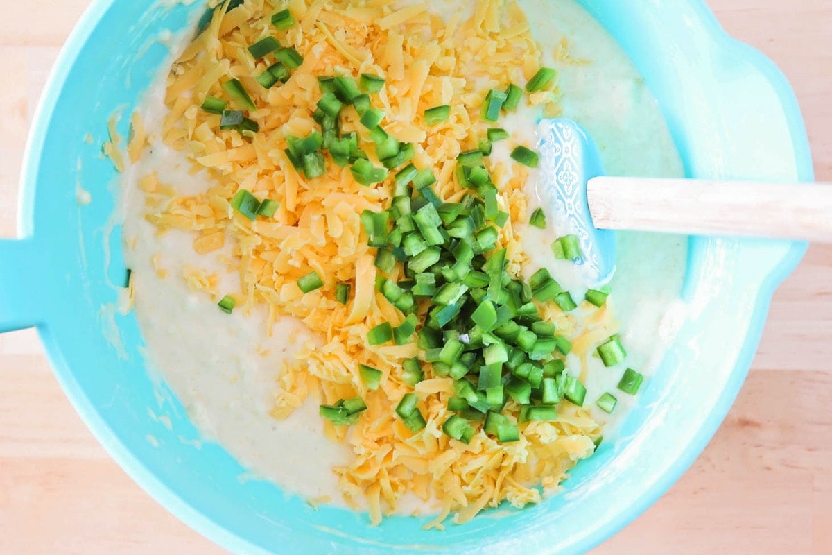 Adding shredded cheese and diced jalapenos to a batter of cornmeal.