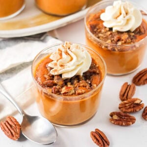 Pumpkin custard in glass cups with pecans and whipped cream.
