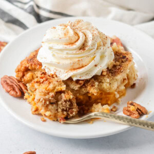 Pumpkin Dump Cake slice on white plate with whipped cream on top.
