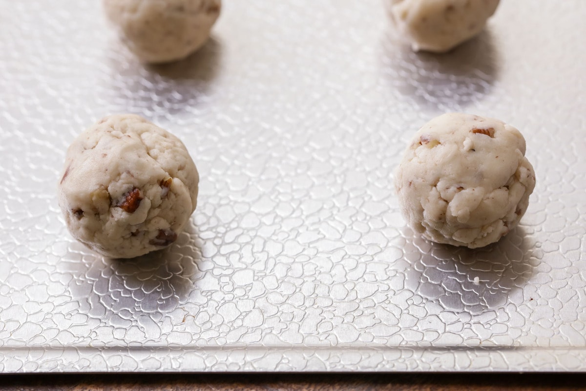 Snowball Cookie dough balls with Pecans on cookie sheet.