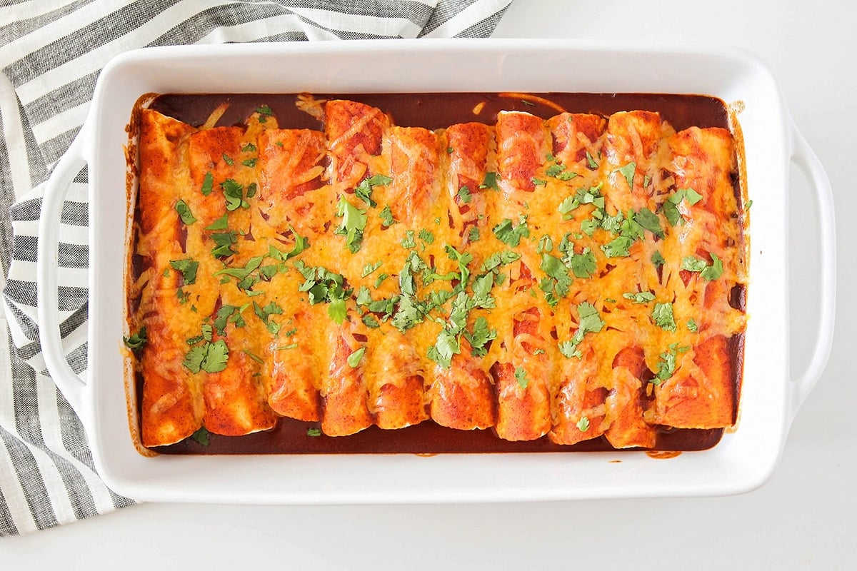 A pan full of enchiladas topped with cheese.