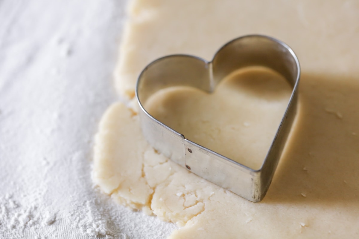 cookie dough on a floured surface with a heart shaped cookie cutter