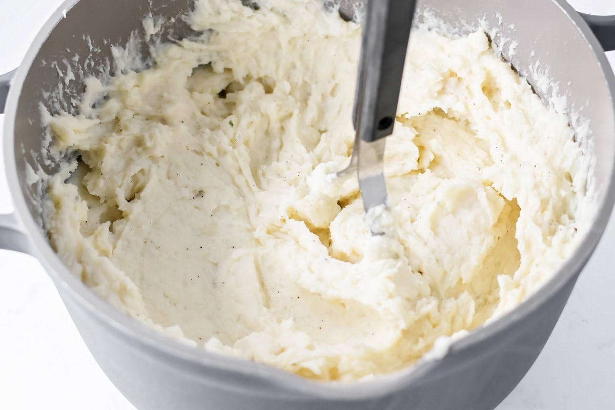Mashed potatoes being mashed in mixing bowl.