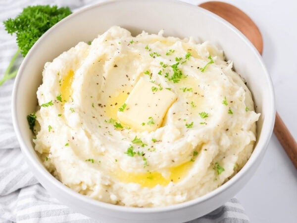 Best mashed potatoes recipe dished into bowl with butter and chives on top.