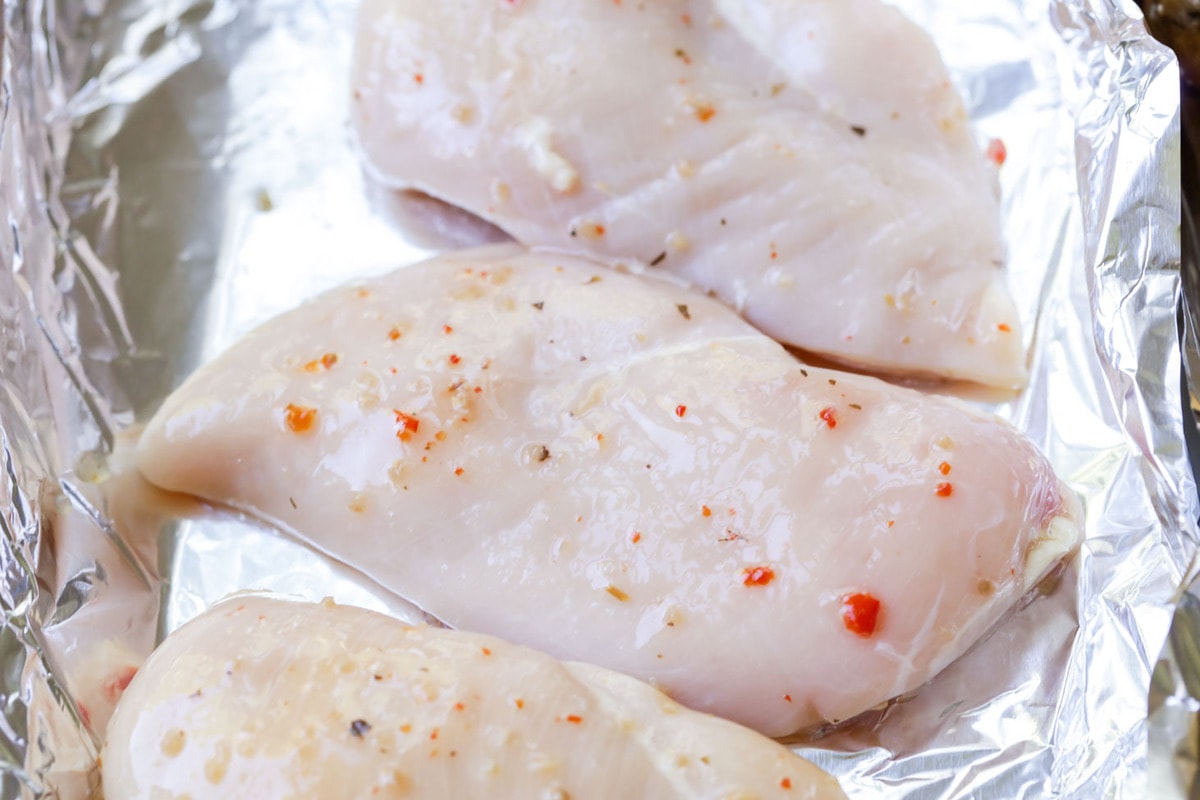 Raw seasoned chicken breast on a lined baking sheet.