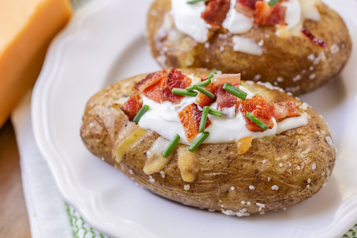 A close up pic of a perfect baked potato topped with sour cream and bacon.
