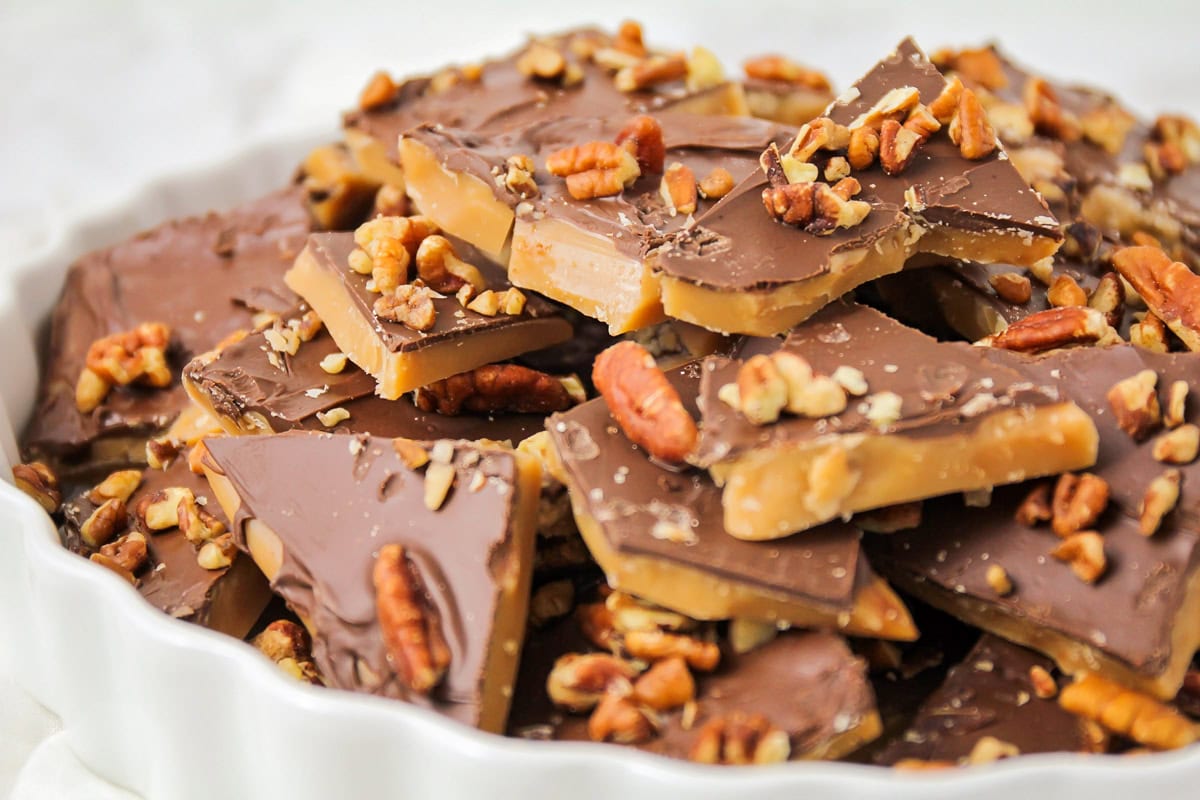 Close up image of homemade Toffee recipe broken into pieces in white dish.