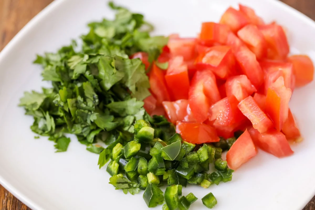 Chopped jalapenos, tomatoes, and cilantro on a plate.