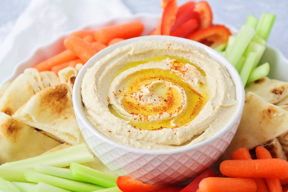 A bowl of hummus surrounded by veggies and pita.