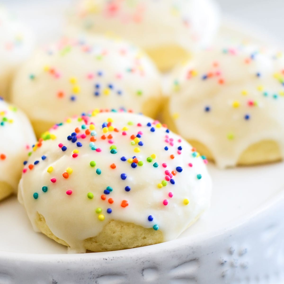 Italian Anise Cookies dipped in glaze and covered in sprinkles on a white plate
