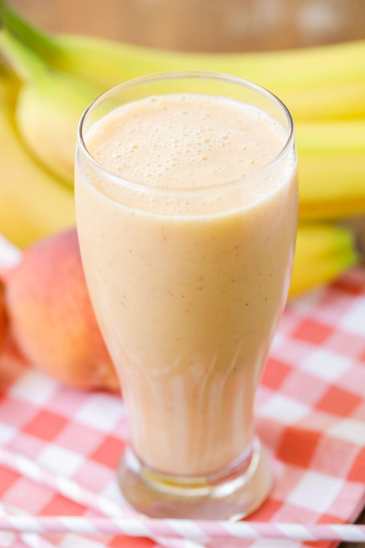 Tall glass of a sweet peach smoothie with fresh fruit in the background.