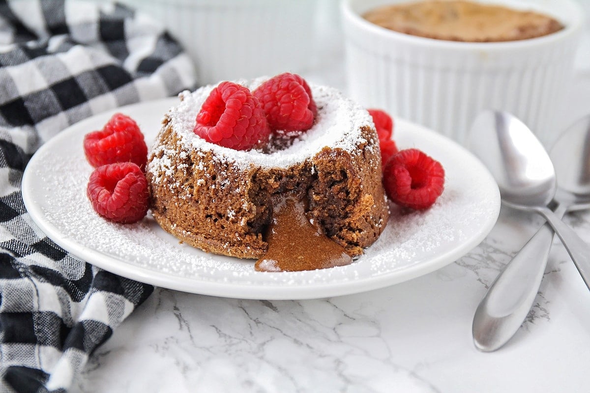 Valentine's Day Desserts - Chocolate Lava Cake topped with powdered sugar and raspberries on a white plate. 