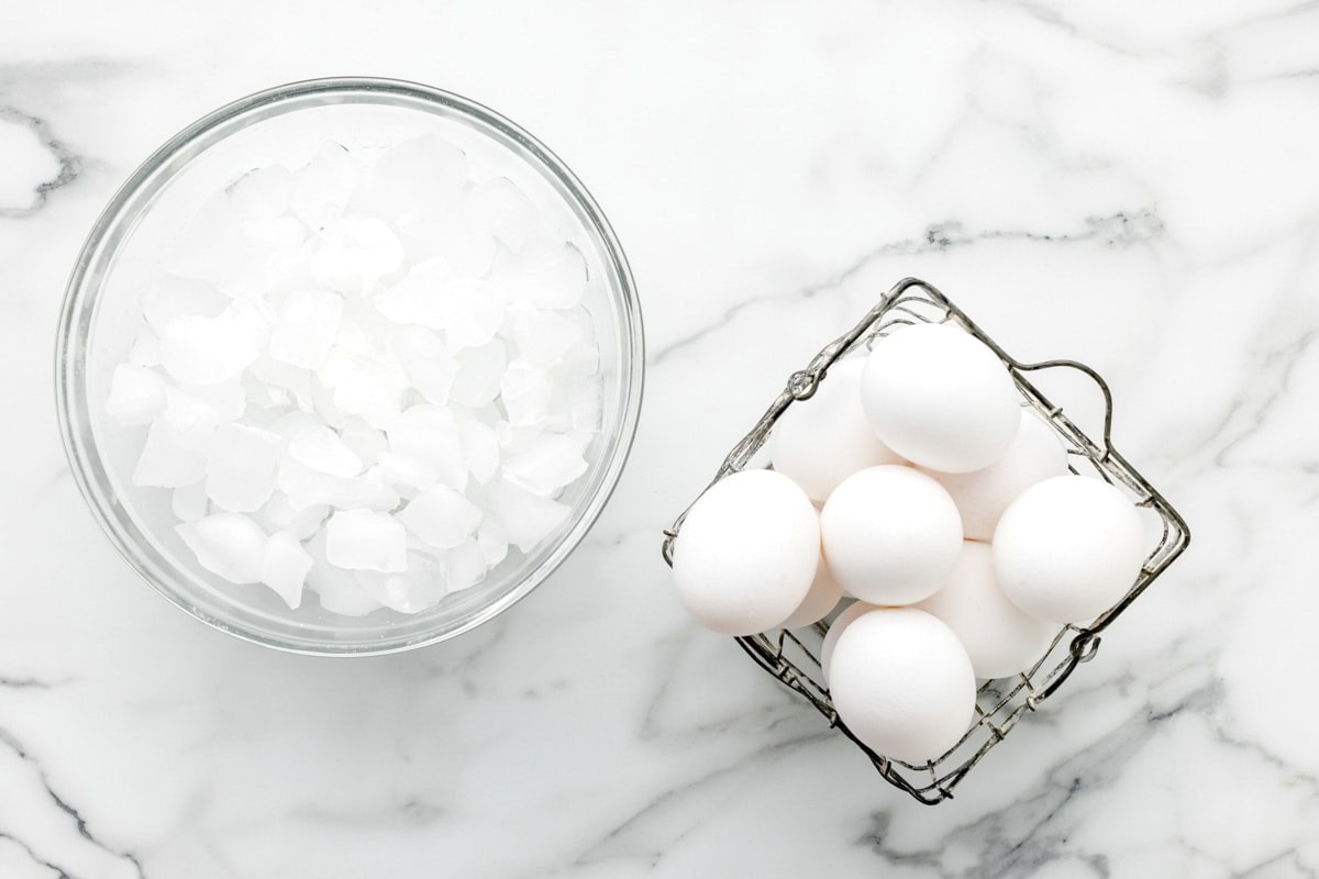 A bowl of ice water next to a basket of eggs.