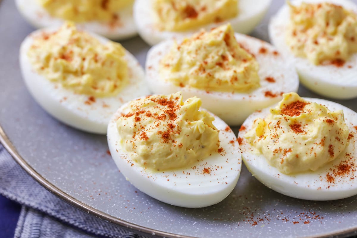 Deviled eggs sprinkled with paprika on a grey plate with a silver rim. 