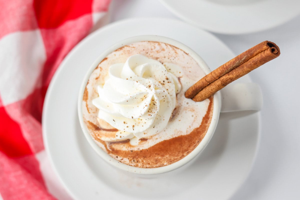 Mexican hot chocolate poured into cup with whipped cream and cinnamon stick on top.