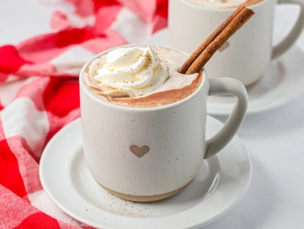 Mexican hot chocolate recipe in cup with cinnamon stick and whipped cream.