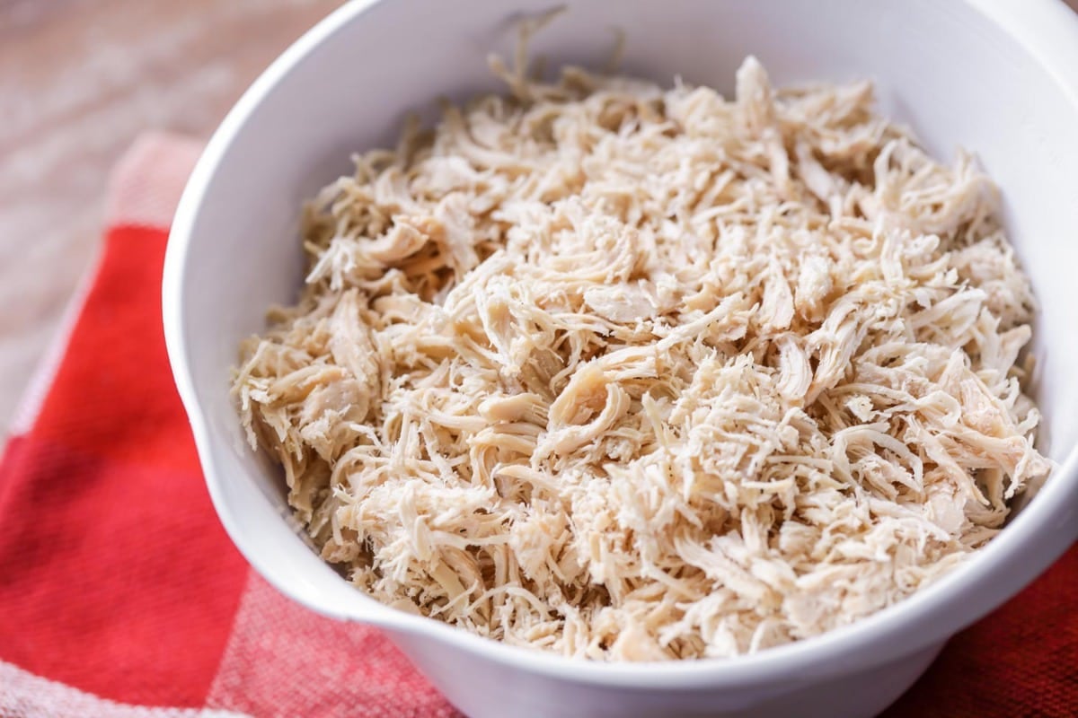 A white mixing bowl full of shredded chicken.