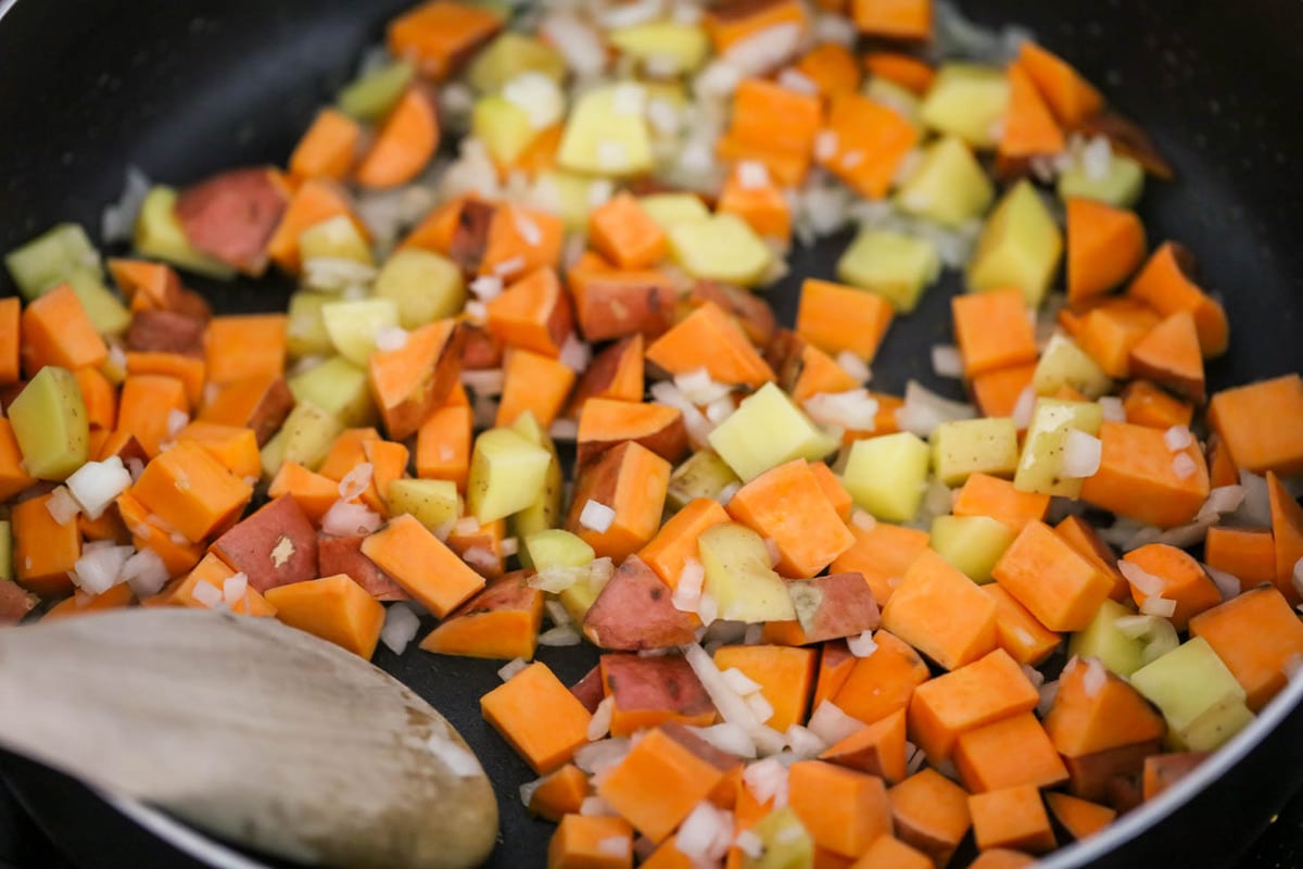 Cooking sweet potatoes and onions in a pan for sweet potato hash.