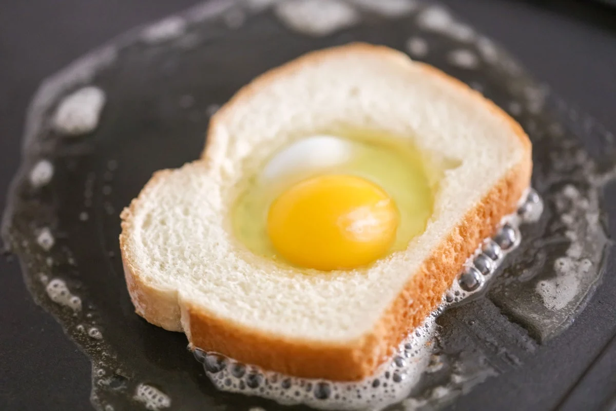 Bread with an egg in the middle, toasting in a pan for toad in a hole breakfast.