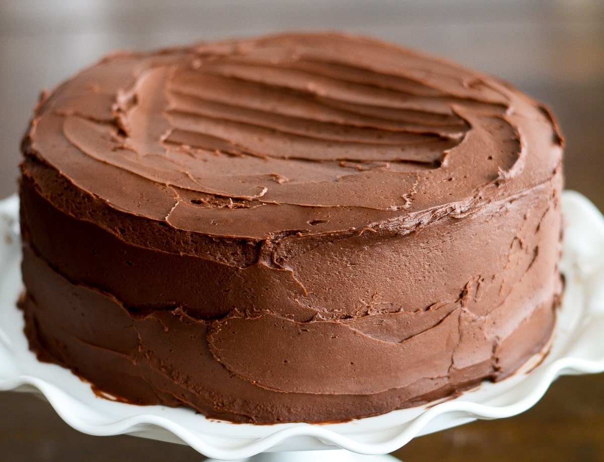 Frosted chocolate cake on a white cake stand.