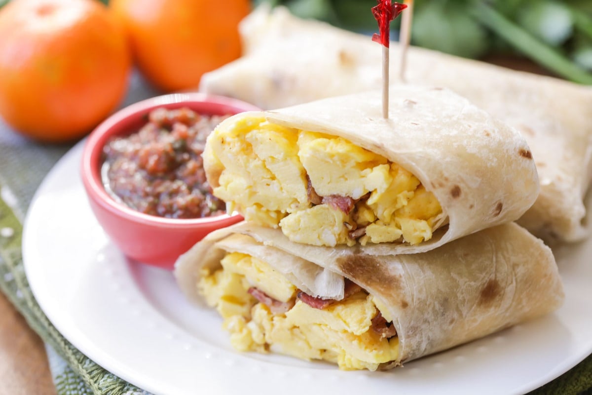 Breakfast Egg Recipes - breakfast burrito cut in half with a side of red salsa on a white plate. 