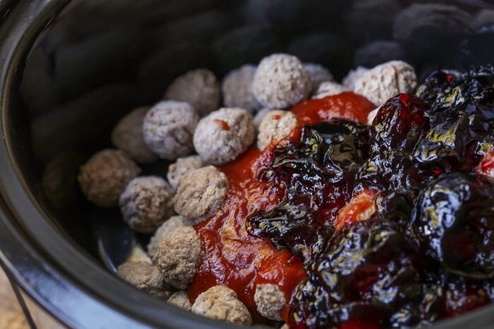 Just three ingredients to make our sweet & tangy dump-and-go grape jelly meatballs - minutes to prep for the perfect dinner or appetizer! Dumping all grape jelly meatballs ingredients into a crock pot.