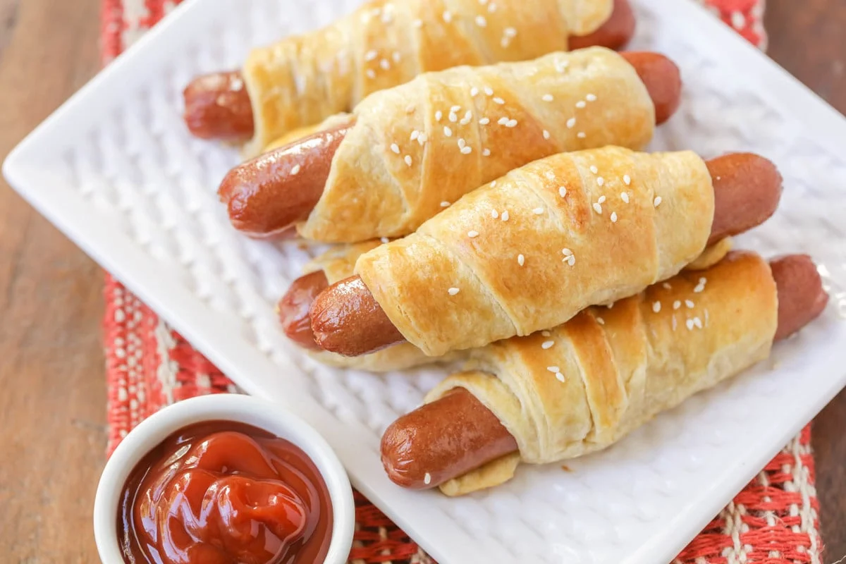 Pigs in a Blanket on white dish served with a side of ketchup.