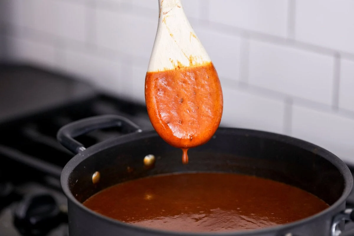 Thick enchilada sauce coating the back of a wooden spoon.