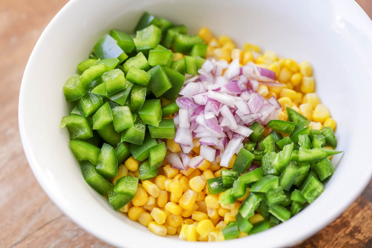 Corn, chopped onion, peppers, and jalapenos in a white bowl.